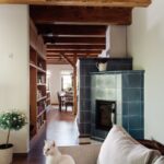 Moderná modrá kachľová pec ma chodbe so vstavanou drevenou policou a dreveným trámovým stropom.