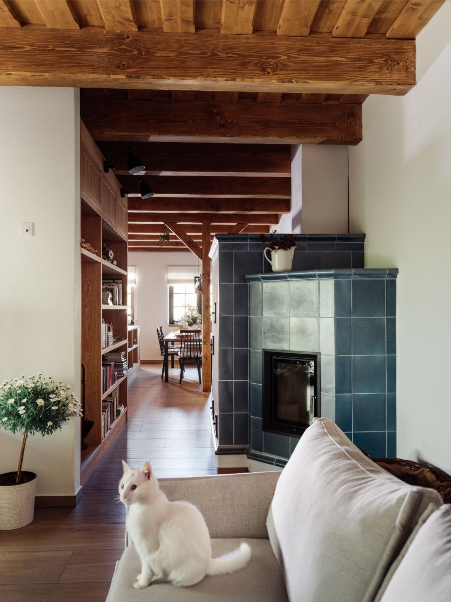 Moderná modrá kachľová pec ma chodbe so vstavanou drevenou policou a dreveným trámovým stropom.