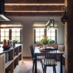 Drevený jedálenský stôl s čiernymi stoličkami pri oknách s béžovými rímskymi roletami v chalupárskom štýle.