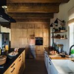 Kuchynský ostrov s masívnymi zásuvkami a čiernou varnou plochou v interiéri s rustikálnym stropom.