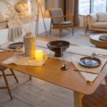 Drevený jedálenský stôl s ľanovým prestieraním, kameninovou vázou a svetlými retro stoličkami v škandinávskom štýle.