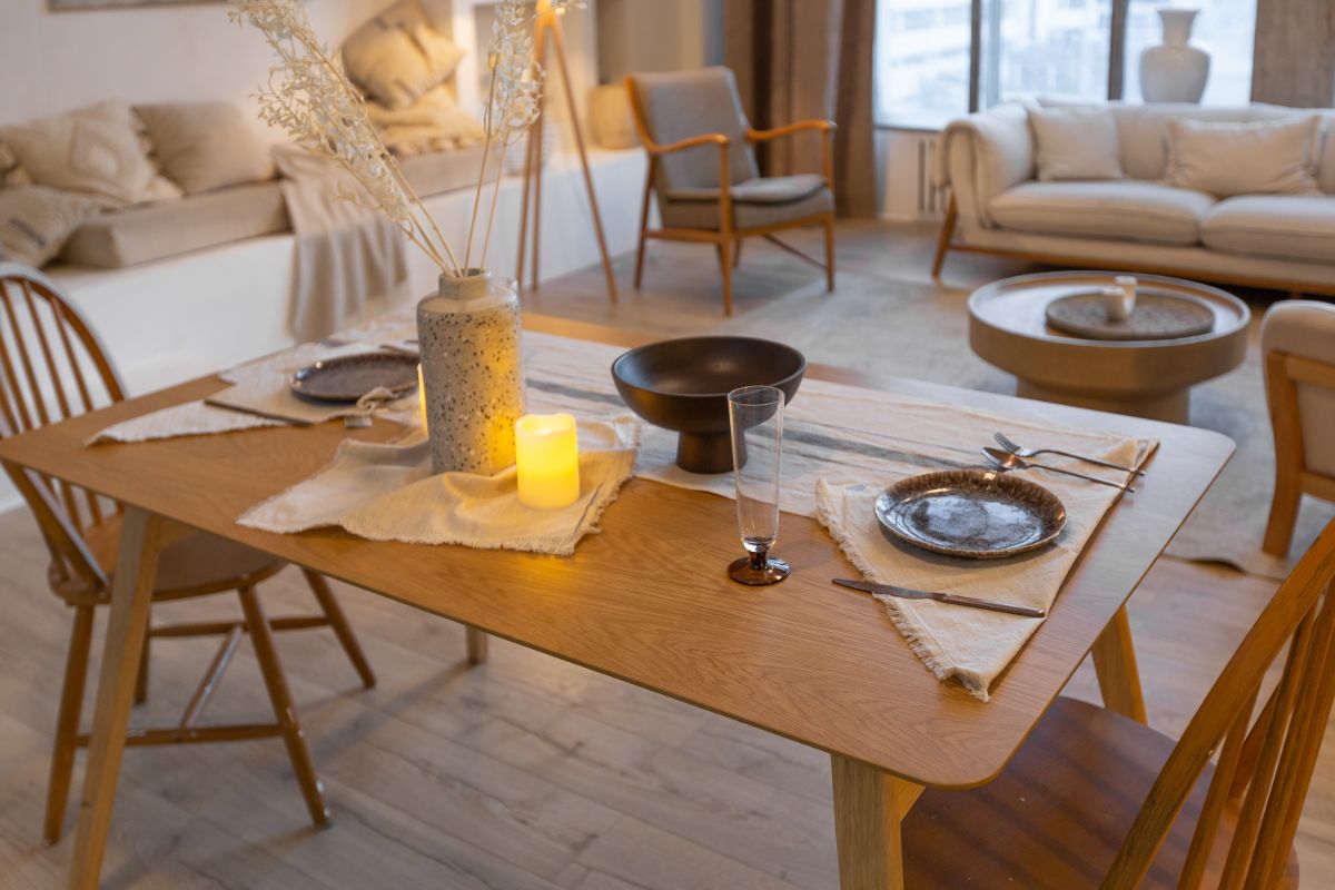 Drevený jedálenský stôl s ľanovým prestieraním, kameninovou vázou a svetlými retro stoličkami v škandinávskom štýle.