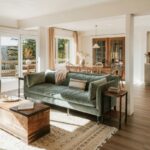 Otvorený vidiecky priestor so zamatovou zelenou pohovkou, masívnym dreveným stolíkom a prírodným tkaným kobercom.