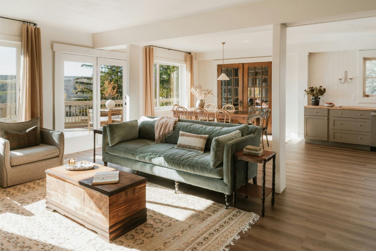 Otvorený vidiecky priestor so zamatovou zelenou pohovkou, masívnym dreveným stolíkom a prírodným tkaným kobercom.