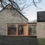 Vidiecky dom so sedlovou strechou, kamennou fasádou a veľkoformátovým oknom s dreveným rámom.