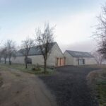 Moderná vidiecka usadlosť s kamennými múrmi, šedou sedlovou strechou a príjazdovou cestou z tmavého kameniva.