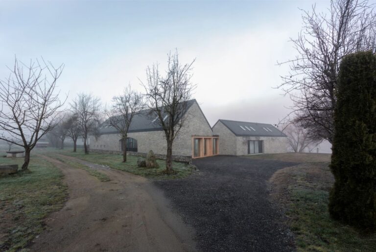 Moderná vidiecka usadlosť s kamennými múrmi, šedou sedlovou strechou a príjazdovou cestou z tmavého kameniva.