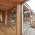 Celodrevené schodisko so skleneným zábradlím vedľa hladkého obkladu stien a priestranná krytá terasa za oknom.