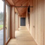 Presvetlená chodba pod šikmým dreveným podhľadom s vertikálnym latovaním stien a tmavými minimalistickými dverami.