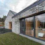 Fasáda z prírodného lámaného kameňa s veľkoformátovým oknom cez ktoré vidno do kúpeľne.