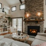 Vysoký kozub s kamenným obložením vedľa krémovej sedačky s dreveným konferenčným stolíkom a bielou vstavanou knižnicou.