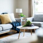 Sedačka so žltým vankúšom, a modrou dekou pri okrúhlom konferenčnom stolíku.