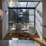 Presklený čierny ateliérový výklenok, biele kožené kreslo, drevená lavica a dubové parkety v tvare rybej kosti.