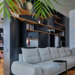 Svetlosivá modulárna pohovka s čiernym kovovým stolíkom pred tmavou nábytkovou zostavou pod betónovým stropom.