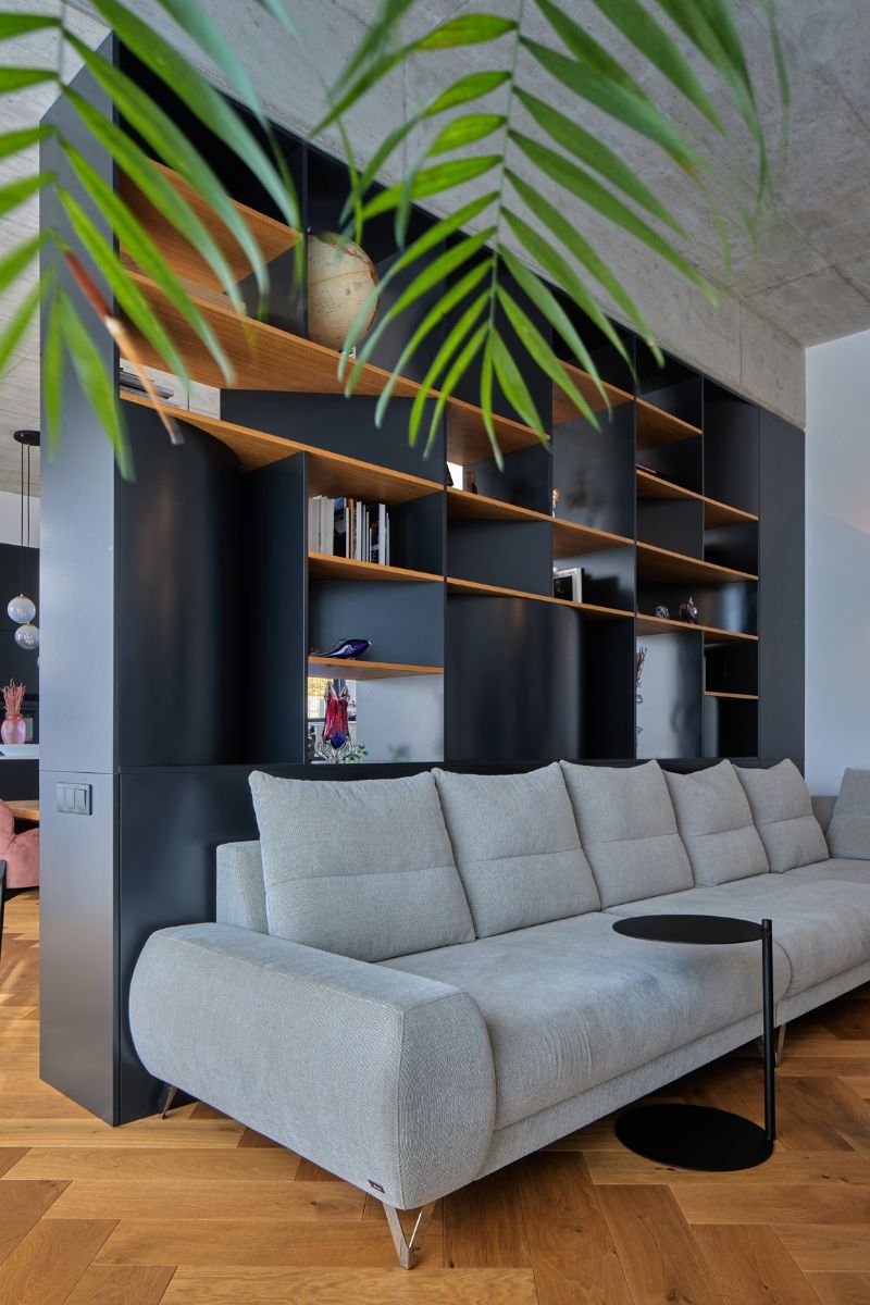 Svetlosivá modulárna pohovka s čiernym kovovým stolíkom pred tmavou nábytkovou zostavou pod betónovým stropom.