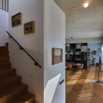 Pohľad do obývacej izby s čiernou policovou zostavou a parketami a schody vedúce na poschodie.