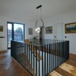 Horné poschodie s čiernym kovovým zábradlím schodiska v presvetlenej hale.