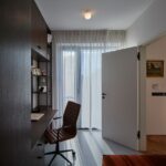 Úzka domáca pracovňa s tmavým dreveným nábytkom a hnedou koženou stoličkou.