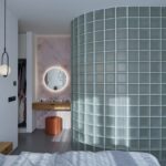 blá stena z matných sklobetónových tvárnic v spálni s ružovou mramorovou stenou a podsvieteným okrúhlym zrkadlom.