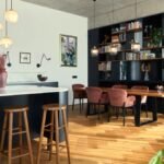 Čierny kuchynský ostrov s bielou mramorovou doskou vedľa jedálenského stola s ružovými zamatovými stoličkami.