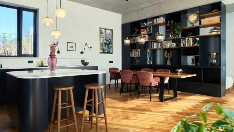 Čierny kuchynský ostrov s bielou mramorovou doskou vedľa jedálenského stola s ružovými zamatovými stoličkami.