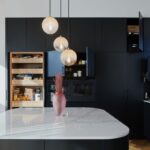 Moderná čierna kuchynská linka s otvorenými skrinkami, ostrovčekom s bielou pracovnou doskou a závesnými svietidlami