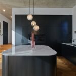 Moderná čierna kuchynská linka s ostrovčekom s bielou pracovnou doskou a závesnými svietidlami