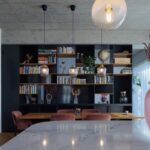 Čierna policová zostava za masívnym dubovým stolom s tromi visiacimi sklenenými lampami.