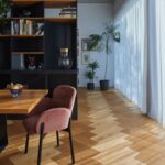 Chodba za dreveným stolom s ružovými čalúnenými stoličkami pri čiernej policovej zostave.