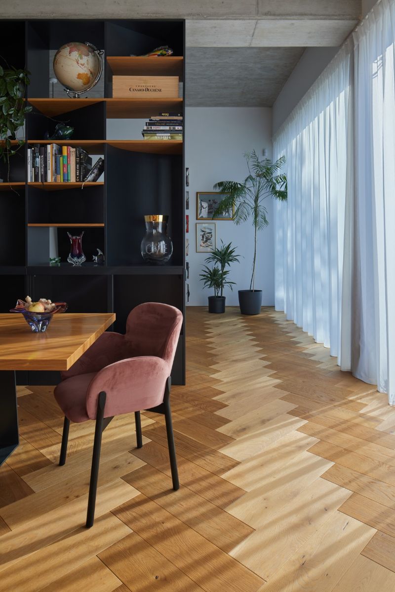 Chodba za dreveným stolom s ružovými čalúnenými stoličkami pri čiernej policovej zostave.