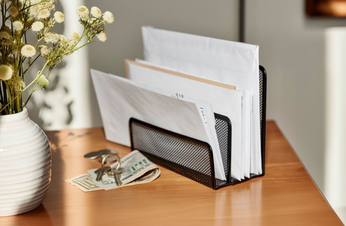 Organizér na poštu na drevenom stolíku vedľa bankoviek, vázy na kvety a kľúčov.