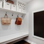 Biela predsieňová stena s drevenou lavicou, čiernymi kovovými háčikmi a vstavanou tabuľou na odkazy.