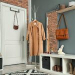 Biela policová lavička s hnedými topánkami a strieborný stojanový vešiak pred tehlovým obkladom.