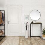 Kovový regál s hnedým sakom, biely tehlový obklad a okrúhle zrkadlo nad moderným stolíkom.