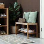 Drevený botník s bielymi teniskami a nízka pletená lavica s modrými vankúšmi pri hnedej stene.