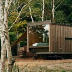 Drevený mobilný dom na oceľovom podvozku s veľkým presklením v hustom brezovom lese.