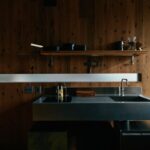 Kuchynská linka s kovovou pracovnou doskou, čiernou varnou doskou a tmavým dreveným obkladom steny.