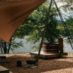 Exteriér mobilného domu s tieniacou plachtou, kúpacou kaďou a malým ohniskom.