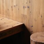 Drevená stena s výraznou textúrou uzlov, kúsok drevenej platformy a valcový drevený stolík.