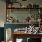 Zelená kuchynská linka s drevenou doskou, biela dizajnová stolička a červená dlažba s bielym geometrickým vzorom.