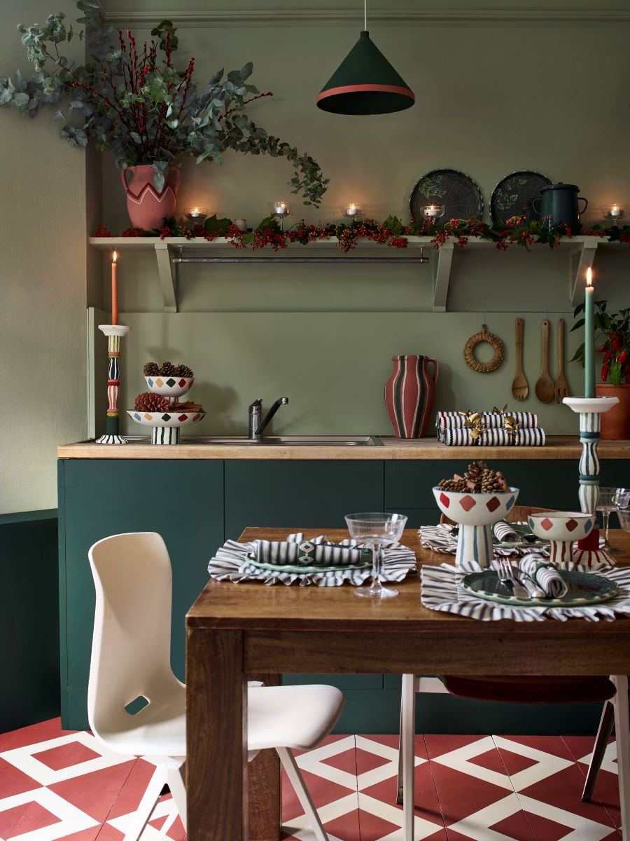 Zelená kuchynská linka s drevenou doskou, biela dizajnová stolička a červená dlažba s bielym geometrickým vzorom.