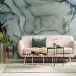 Abstraktná mramorová tapeta, krémová zaoblená sedačka, zlaté kovové stolíky a tmavozelená nízka komoda v obývačke.