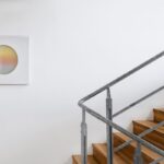 Moderné schodisko s drevenými stupňami, kovovým zábradlím a minimalistickým kruhovým obrazom.