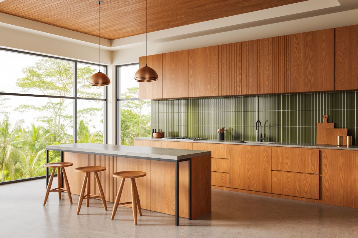 Moderná kuchynská linka v minimalistickom štýle s drevenými skrinkami vo farbe medového dreva, kuchynským ostrovčekom a tmavozelenou zástenou.