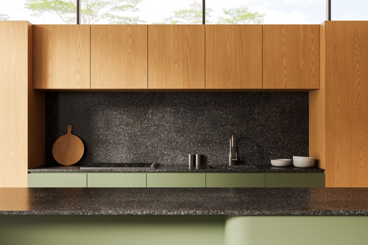 Detail na kuchynskú linku v drevenom dekore v odtieni medového dreva s tmavou zástenou a pracovnou doskou a zelenými dolnými skrinkami.