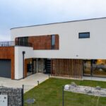 Moderný poschodový dom s bielou fasádou, dreveným lamelovým obkladom a antracitovými rámami okien