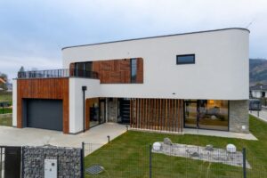 Moderný poschodový dom s bielou fasádou, dreveným lamelovým obkladom a antracitovými rámami okien
