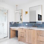 Moderná kúpeľňa s walk-in sprchovým kútom, modrým obkladom, drevenou skrinkou, umývadlom v kamennej doske a zrkadlami.