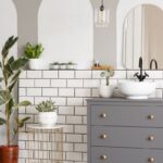 Kúpeľňa s obkladačkami v štýle metro, izbovými rastlinami, sivou komodou s mosadznými úchytmi a umývadlom.