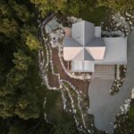 Pohľad zhora na modernú horskú chatu s plechovou strechou, kamennými terasami a prírodným lesným pozemkom.